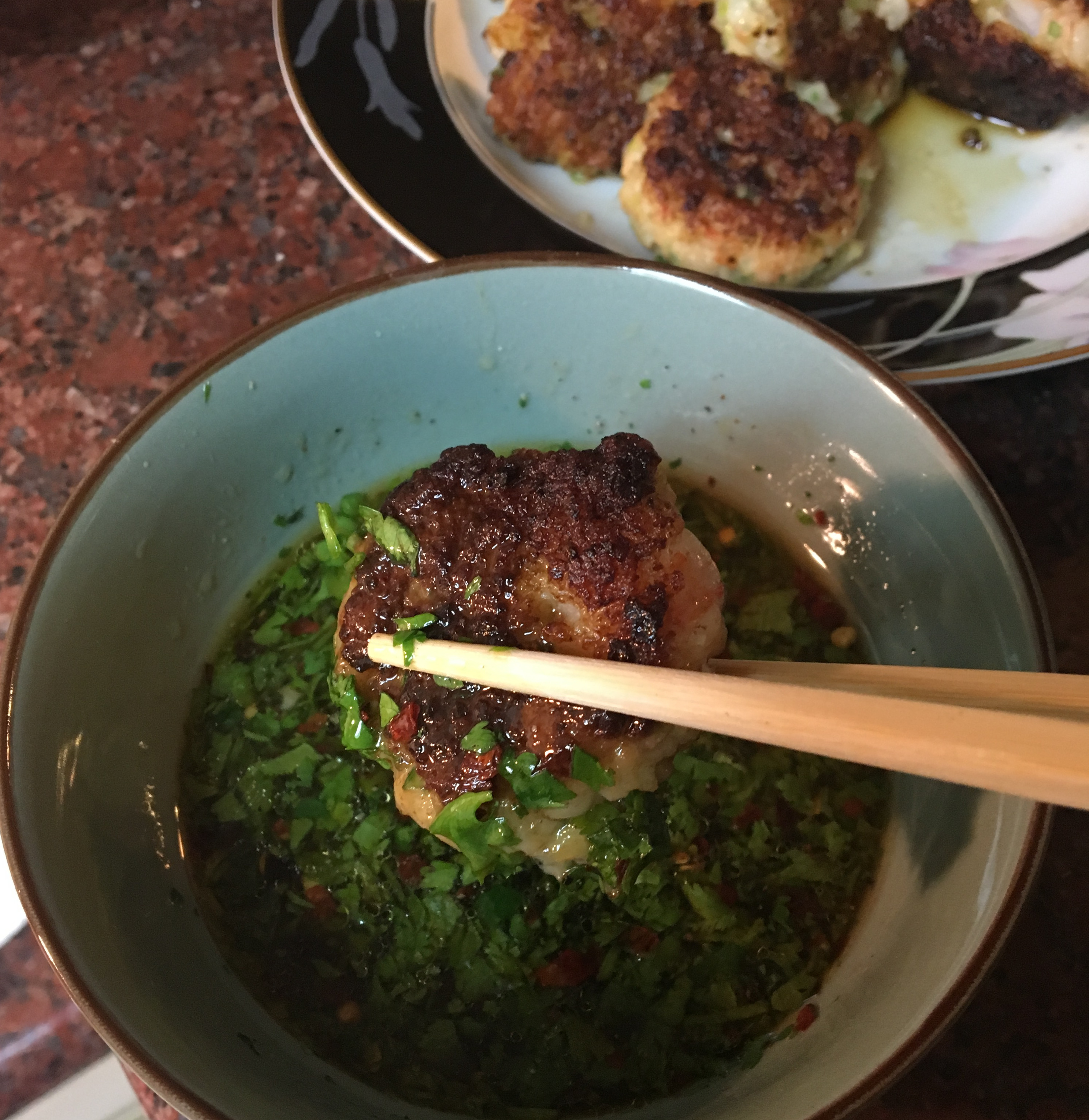 A dumpling being dunked into sauce using a pair of chopsticks. 