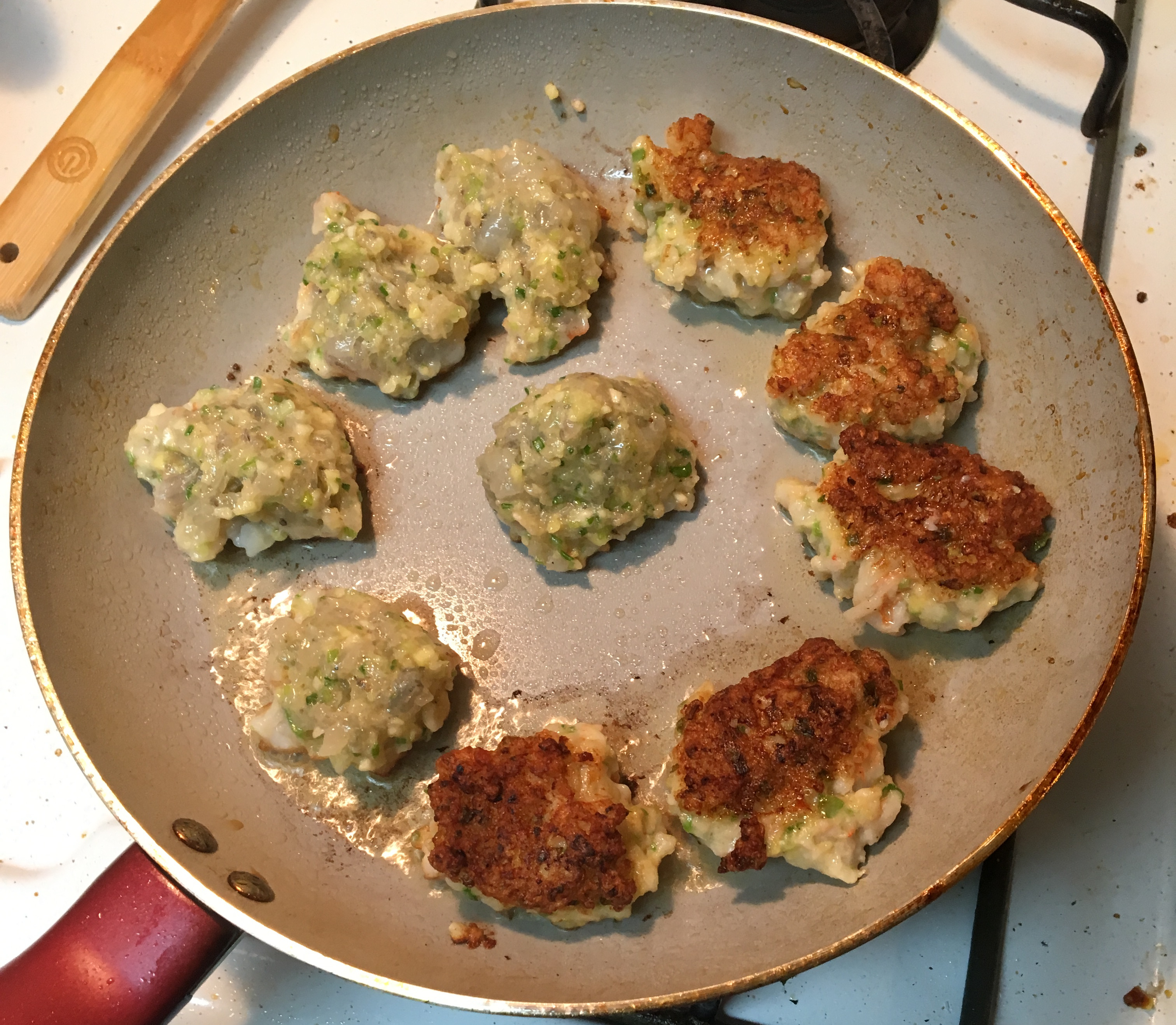 A pan of cooking dumplings, half of them turned over and half waiting to be turned. 