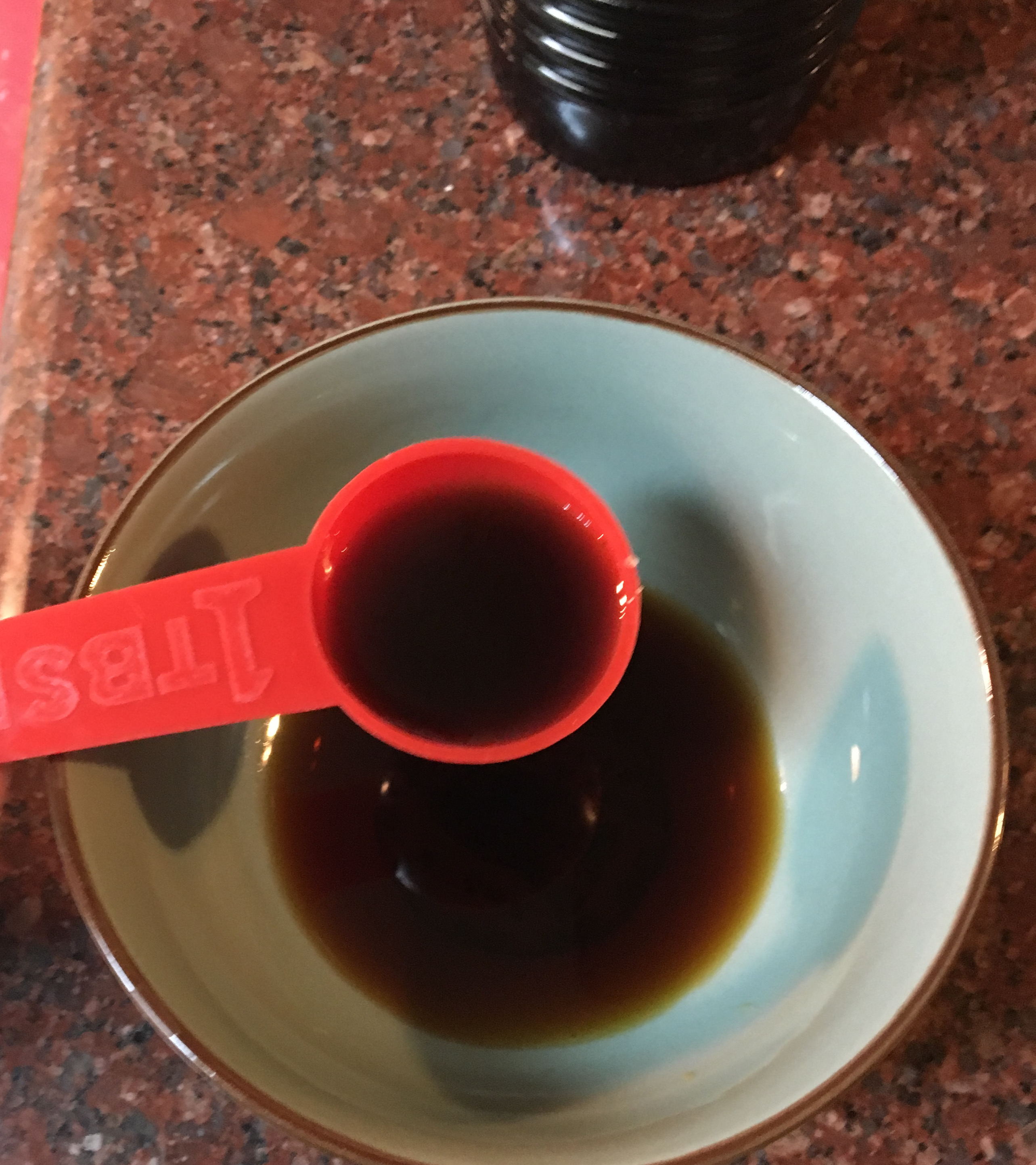 A bowl of soy sauce with a measured tablespoon of sesame oil being added. 